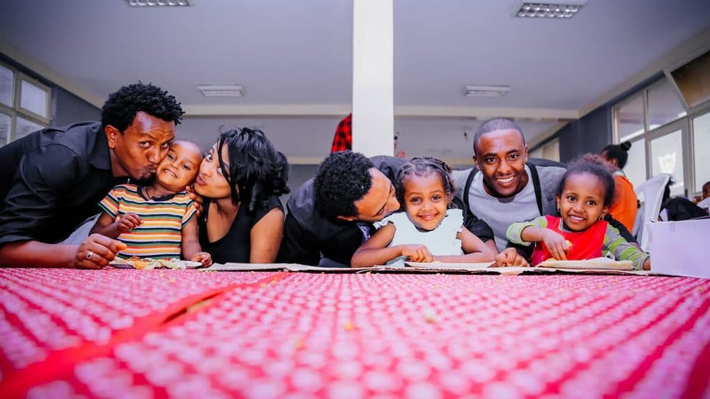 woman and three men with three children on front of desk with red cloth