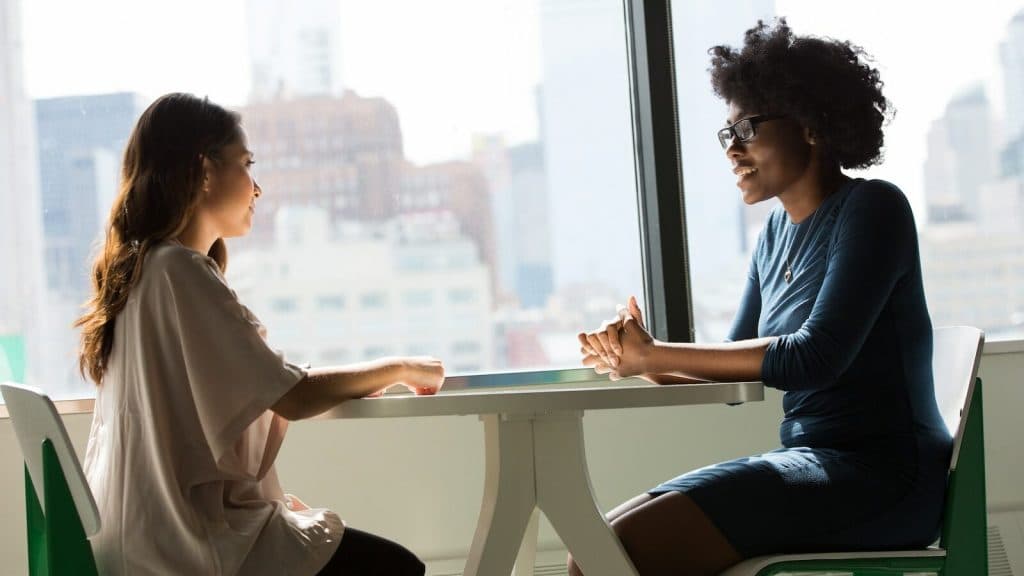 two women sitting beside table and talking